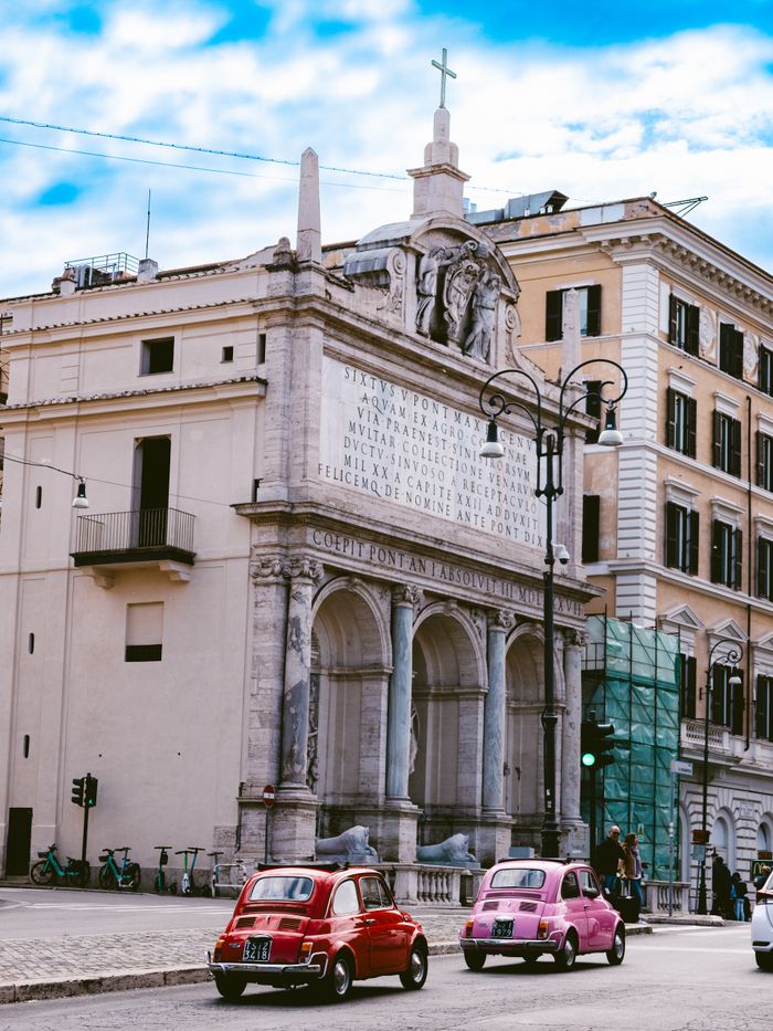 Vintage Fiat cars in front of the historic Fountain of Moses in Rome, Italy, captured on a sunny day.